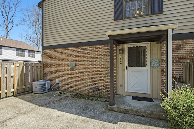 3669 Brentwood St, Norton Shores, MI 49441 - view of exterior entry featuring brick siding, cooling unit, a patio area, and fence