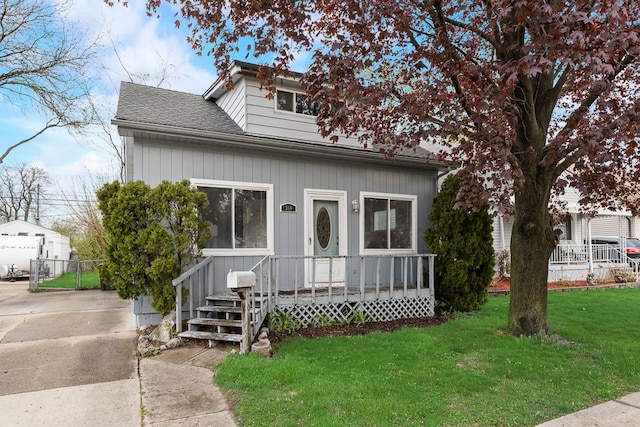 bungalow-style house with fence, a shingled roof, driveway, and a front lawn