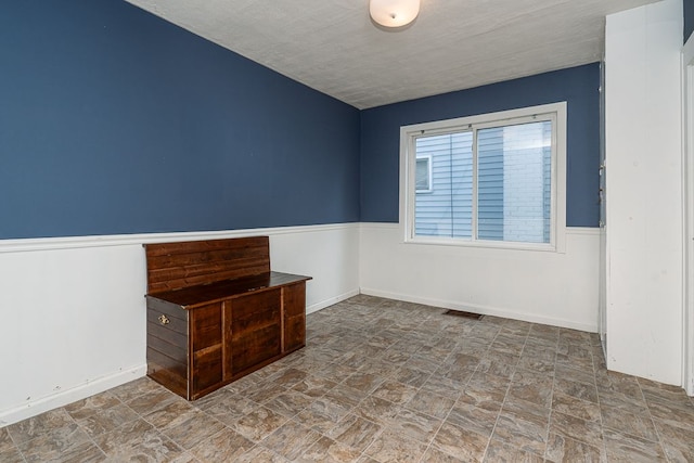 empty room featuring visible vents, wainscoting, and stone finish floor