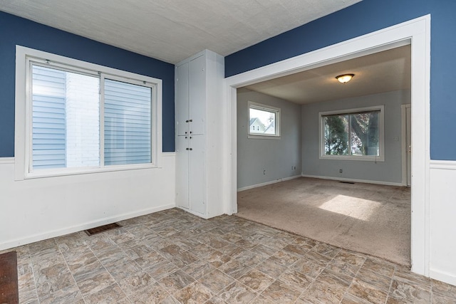 carpeted empty room featuring stone finish flooring, baseboards, and visible vents