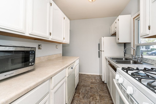 kitchen with a sink, stone finish flooring, white appliances, and white cabinetry