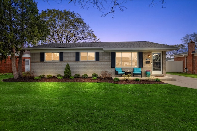ranch-style house featuring a porch, fence, a yard, and brick siding