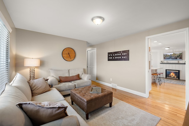 living room with light wood finished floors, visible vents, baseboards, and a fireplace