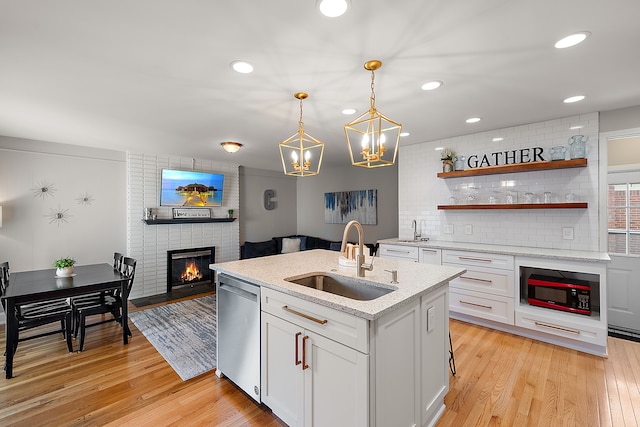 kitchen featuring white cabinetry, stainless steel dishwasher, a sink, built in microwave, and a center island with sink