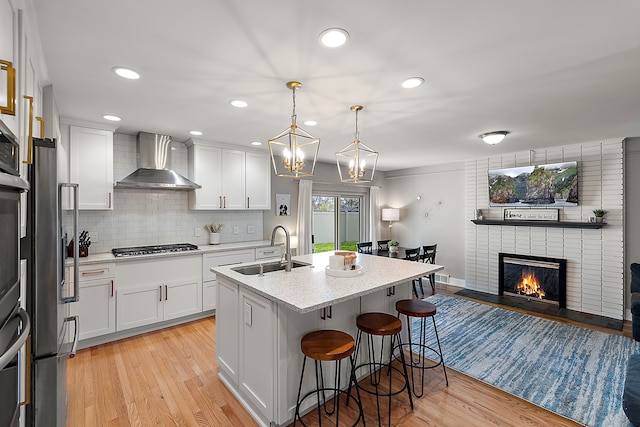 kitchen with a sink, a kitchen breakfast bar, wall chimney exhaust hood, backsplash, and light wood-style flooring