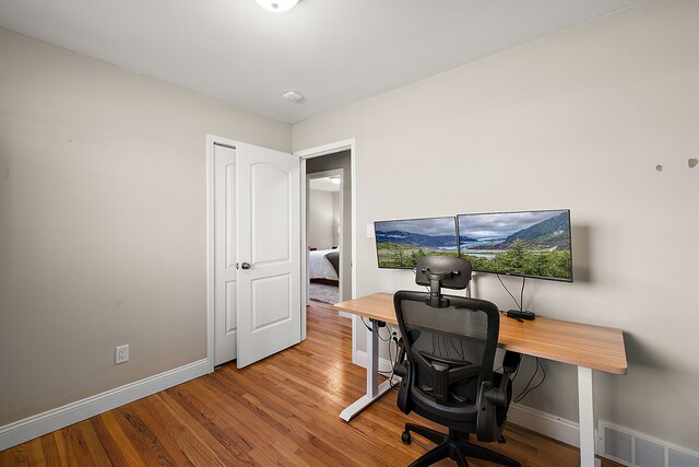 home office with baseboards, visible vents, and wood finished floors