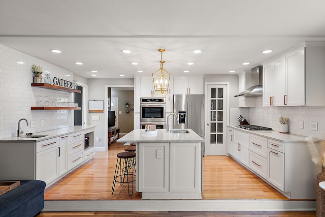 kitchen featuring light wood finished floors, a sink, stainless steel appliances, wall chimney exhaust hood, and backsplash
