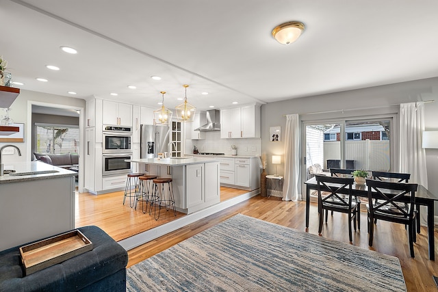 kitchen with a sink, wall chimney range hood, stainless steel appliances, and light wood-style floors