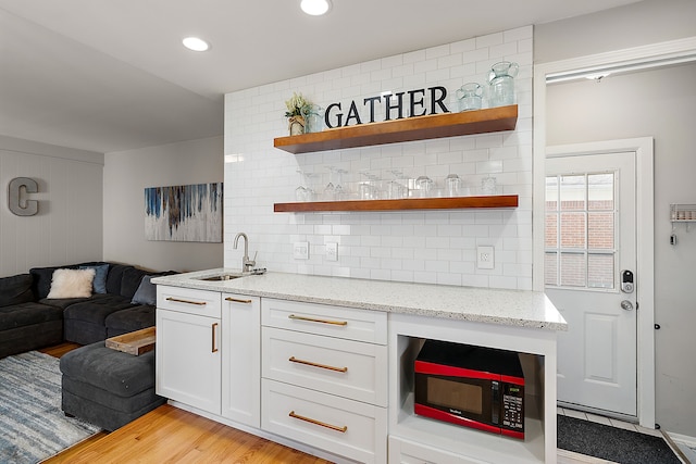 interior space featuring a sink, open shelves, light wood-style flooring, backsplash, and white cabinets