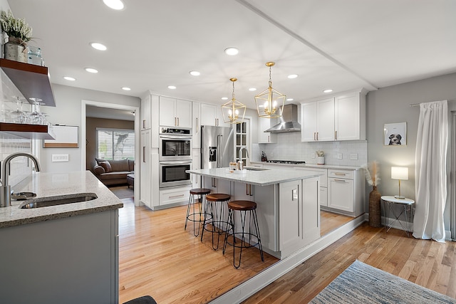 kitchen with wall chimney range hood, tasteful backsplash, stainless steel appliances, and a sink