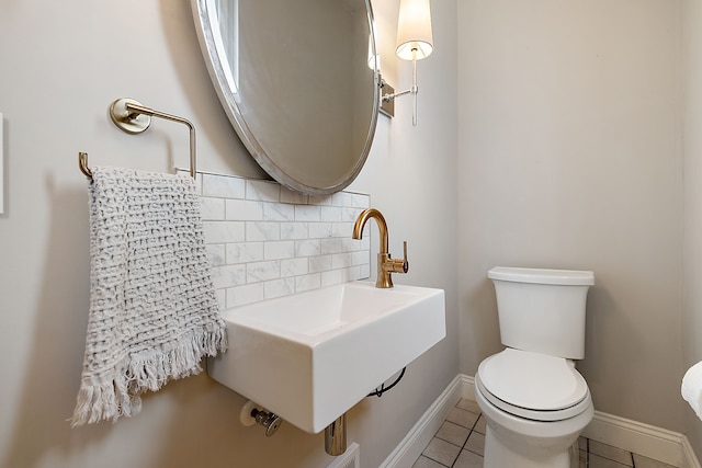 half bath with a sink, tile patterned floors, tasteful backsplash, toilet, and baseboards