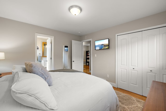 bedroom featuring baseboards, light wood-type flooring, ensuite bath, and a closet