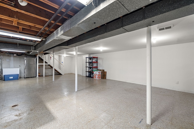 finished basement with visible vents, baseboards, freestanding refrigerator, and stairs