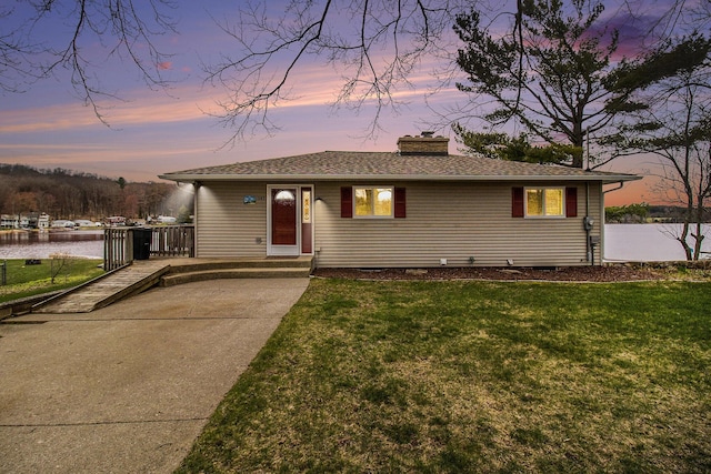 view of front of house featuring a front lawn, roof with shingles, a chimney, and a water view