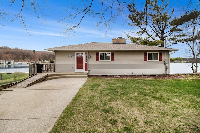 ranch-style home with a chimney, a front lawn, roof with shingles, and a water view
