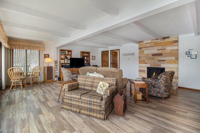 living area with a fireplace, baseboards, beamed ceiling, and light wood-type flooring