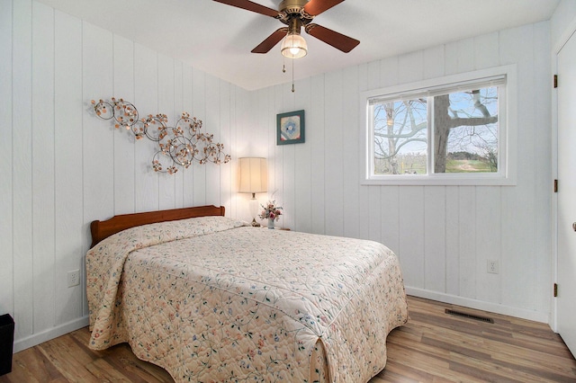 bedroom with wood finished floors, visible vents, a ceiling fan, and baseboards