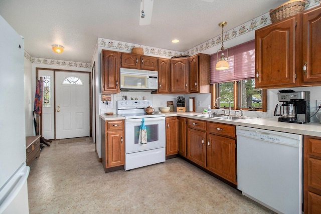 kitchen with a sink, white appliances, brown cabinetry, light countertops, and hanging light fixtures