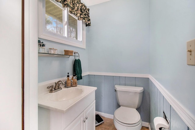bathroom featuring vanity, toilet, and a wainscoted wall