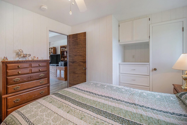 bedroom featuring wood walls, a ceiling fan, and wood finished floors