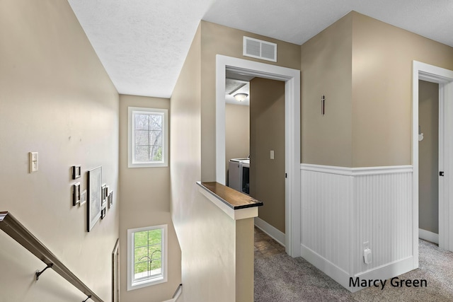 hallway with independent washer and dryer, plenty of natural light, visible vents, and an upstairs landing