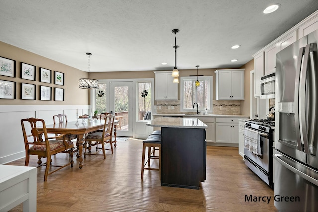 kitchen with a sink, decorative backsplash, a breakfast bar, appliances with stainless steel finishes, and a kitchen island