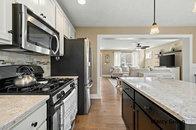 kitchen featuring stainless steel appliances, open floor plan, white cabinetry, decorative backsplash, and a ceiling fan