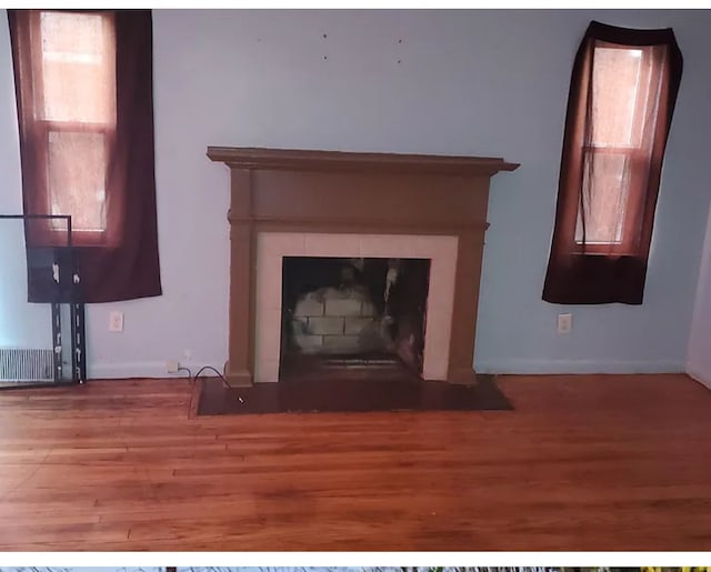 details with baseboards, visible vents, a tiled fireplace, and wood finished floors