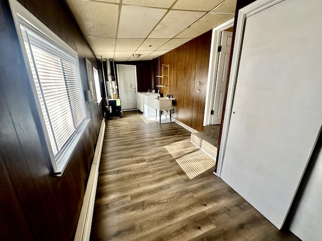corridor with wooden walls, a drop ceiling, and dark wood-style floors