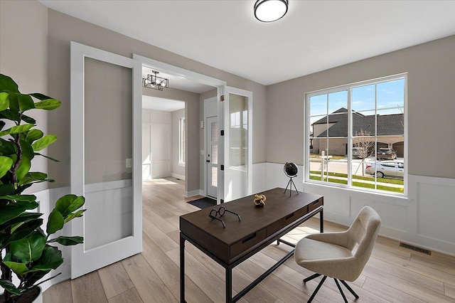 office area with wainscoting, light wood-style flooring, and visible vents