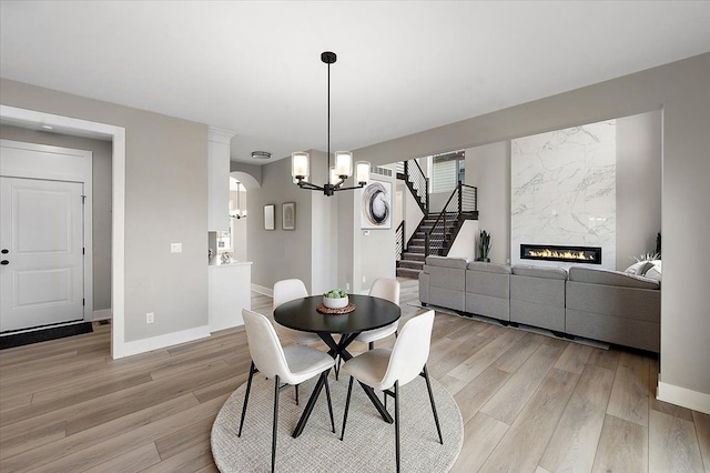 dining room with a high end fireplace, light wood-type flooring, baseboards, and a notable chandelier