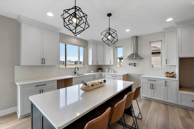kitchen featuring a sink, a healthy amount of sunlight, light wood finished floors, backsplash, and wall chimney exhaust hood