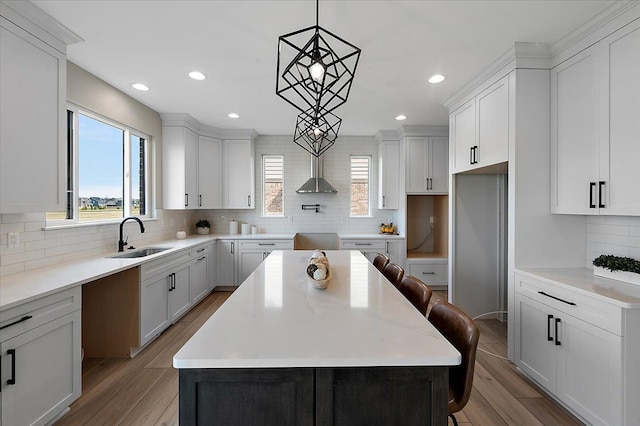 kitchen with a sink, backsplash, wood finished floors, wall chimney range hood, and a kitchen island