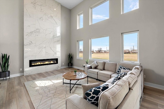 living area with a towering ceiling, baseboards, wood finished floors, and a fireplace