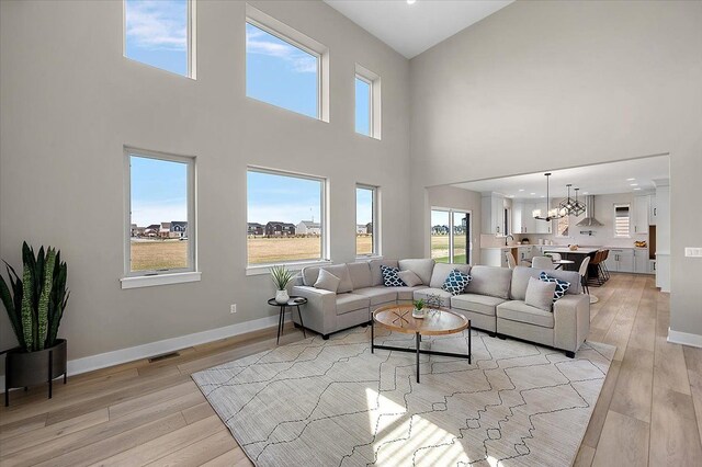 living room featuring light wood finished floors, baseboards, a high ceiling, and an inviting chandelier
