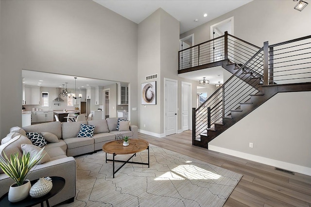 living room featuring baseboards, visible vents, light wood-style floors, a high ceiling, and stairway