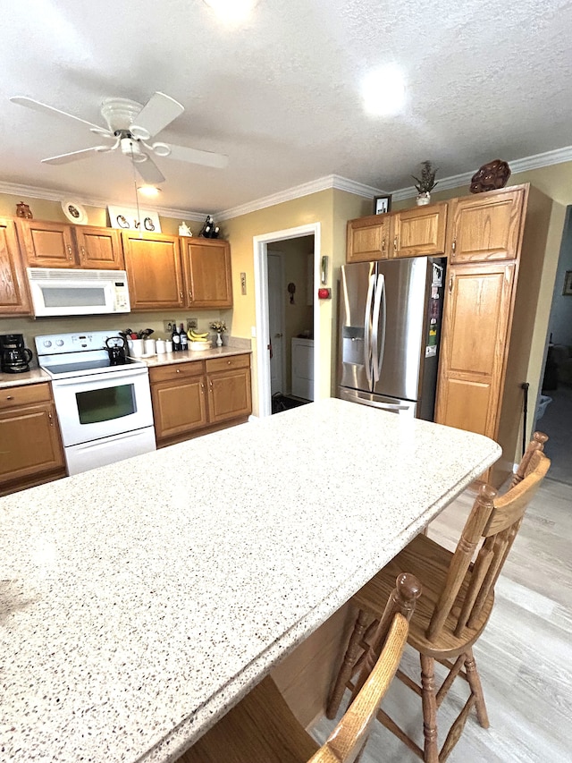 kitchen featuring white appliances, crown molding, light wood-style flooring, and a kitchen bar