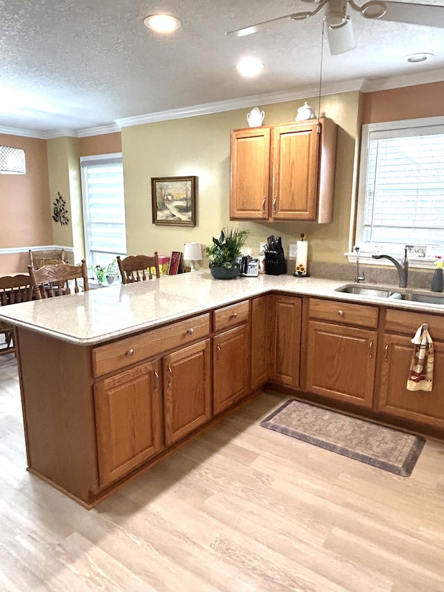 kitchen featuring a peninsula, ceiling fan, a sink, and light wood-type flooring