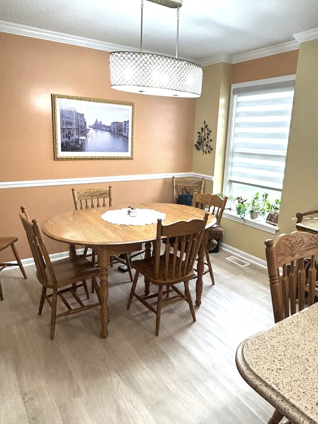 dining room featuring baseboards, ornamental molding, light wood-type flooring, and visible vents