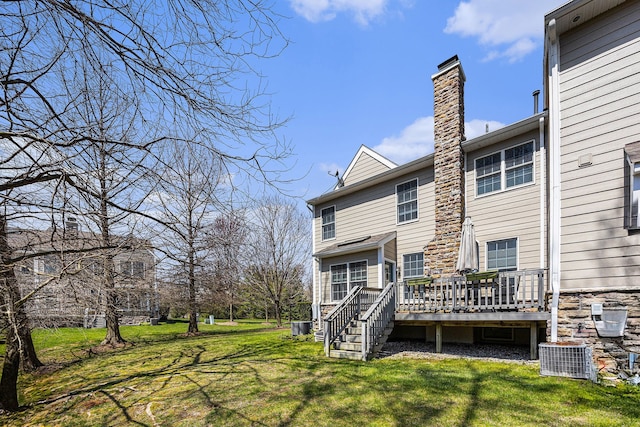 back of property featuring a deck, a chimney, and a lawn