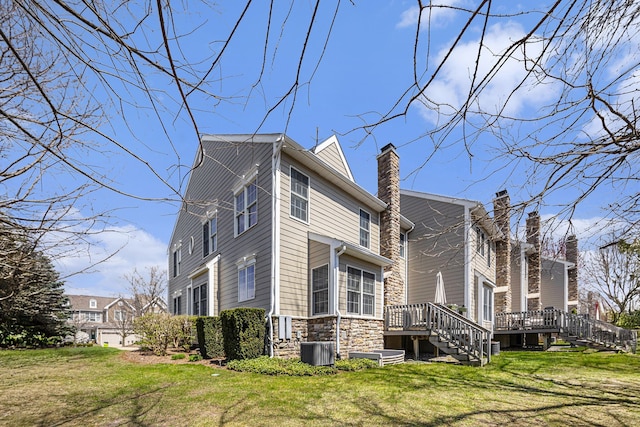 view of side of home with cooling unit, stairs, a wooden deck, stone siding, and a chimney
