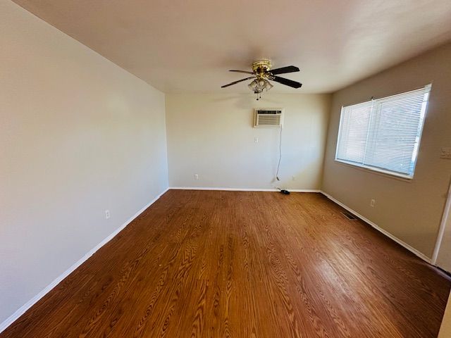 819 Frank Ave, Lincoln Park, MI 48146 - unfurnished room featuring baseboards, a wall mounted air conditioner, wood finished floors, and a ceiling fan
