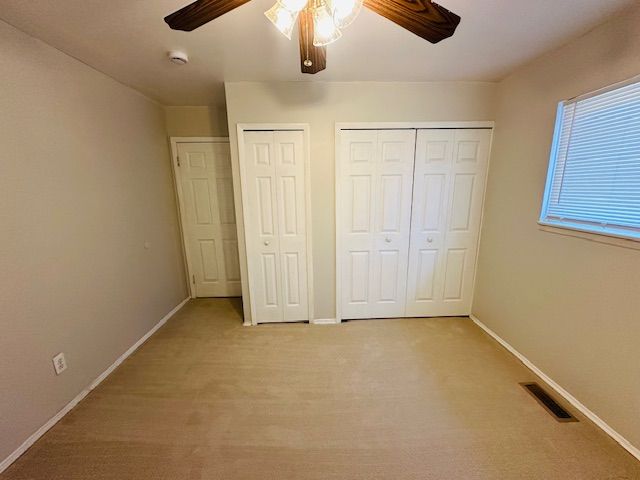 819 Frank Ave, Lincoln Park, MI 48146 - unfurnished bedroom with two closets, light carpet, ceiling fan, baseboards, and visible vents