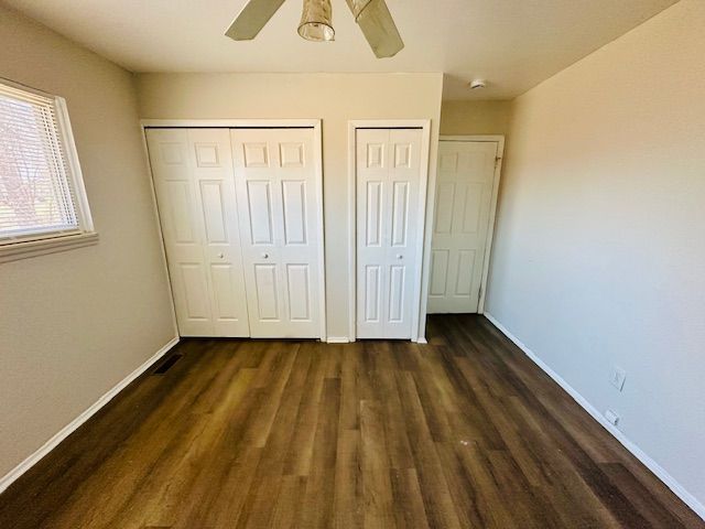 819 Frank Ave, Lincoln Park, MI 48146 - unfurnished bedroom with dark wood finished floors, baseboards, a ceiling fan, and two closets