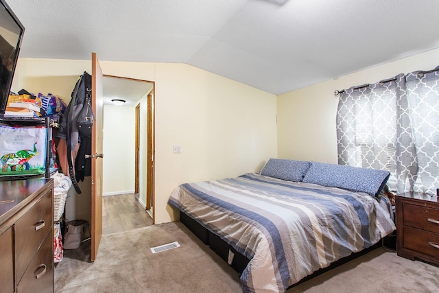 bedroom featuring visible vents, lofted ceiling, and light carpet