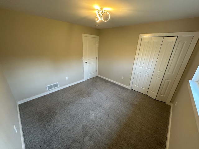 unfurnished bedroom with a closet, dark colored carpet, visible vents, and baseboards