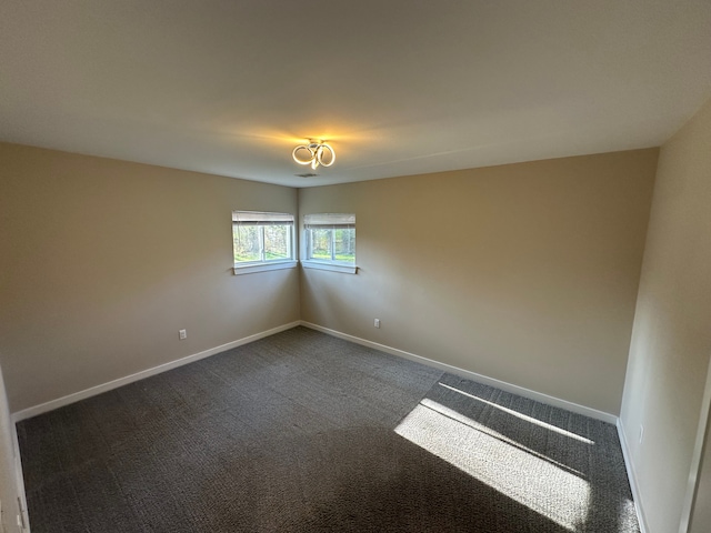 empty room featuring dark colored carpet and baseboards