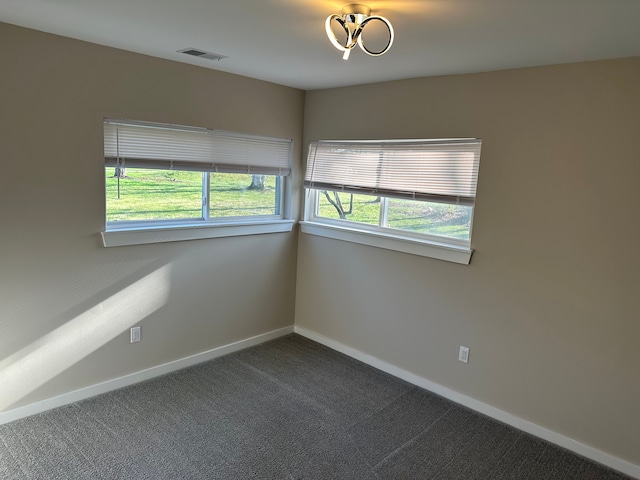 spare room featuring visible vents, dark colored carpet, and baseboards
