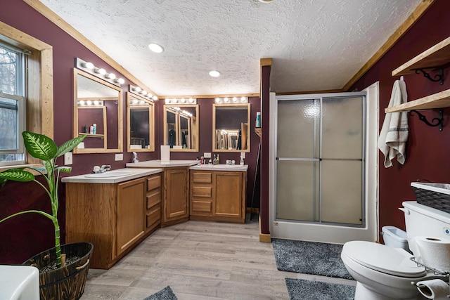 full bathroom with double vanity, wood finished floors, a sink, a textured ceiling, and a stall shower