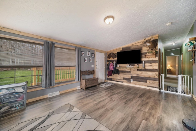 unfurnished living room with a textured ceiling, vaulted ceiling, visible vents, and wood finished floors